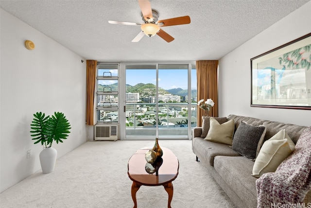 living room with ceiling fan, light colored carpet, a wall of windows, and a textured ceiling