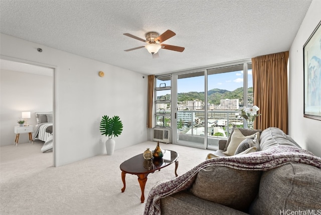 living area with a textured ceiling, ceiling fan, a wall of windows, and light carpet