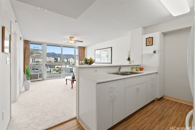 kitchen featuring kitchen peninsula, a textured ceiling, sink, light hardwood / wood-style flooring, and white cabinets