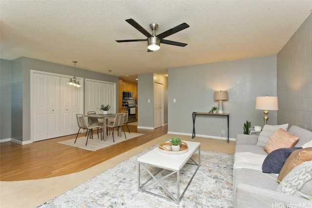 living room with light wood-type flooring, a textured ceiling, and ceiling fan