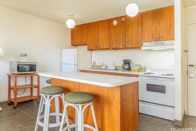 kitchen featuring a textured ceiling, white appliances, sink, a kitchen island, and a breakfast bar area