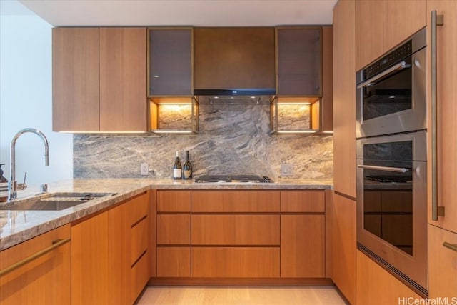 kitchen featuring stainless steel appliances, decorative backsplash, light wood-type flooring, light stone counters, and sink