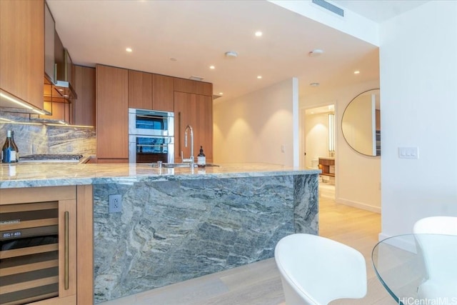 kitchen featuring appliances with stainless steel finishes, wine cooler, sink, light stone counters, and light hardwood / wood-style flooring