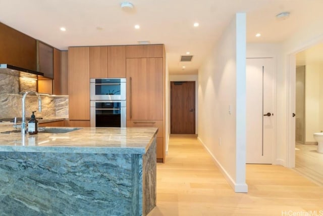 kitchen featuring decorative backsplash, sink, light wood-type flooring, double oven, and light stone counters