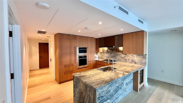 kitchen with visible vents, a sink, light wood-style flooring, and tasteful backsplash