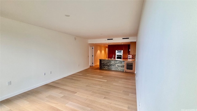 unfurnished living room with light wood-type flooring, baseboards, wine cooler, and visible vents
