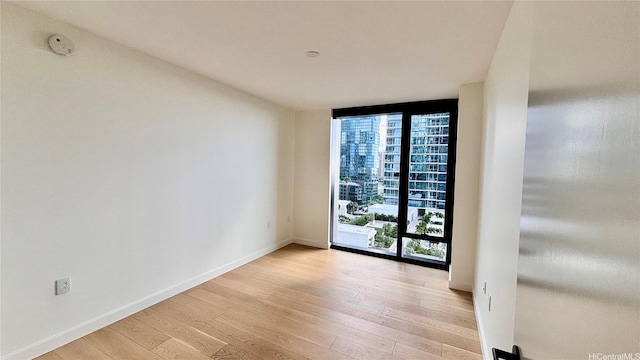 spare room featuring light wood-style floors, floor to ceiling windows, and baseboards