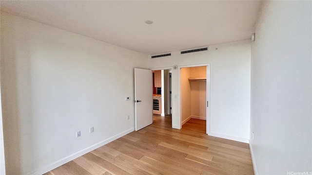 unfurnished bedroom featuring baseboards, visible vents, a walk in closet, and light wood finished floors