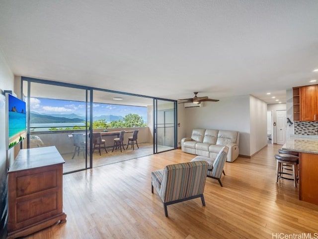 living room featuring a wall mounted AC, light wood-type flooring, and ceiling fan