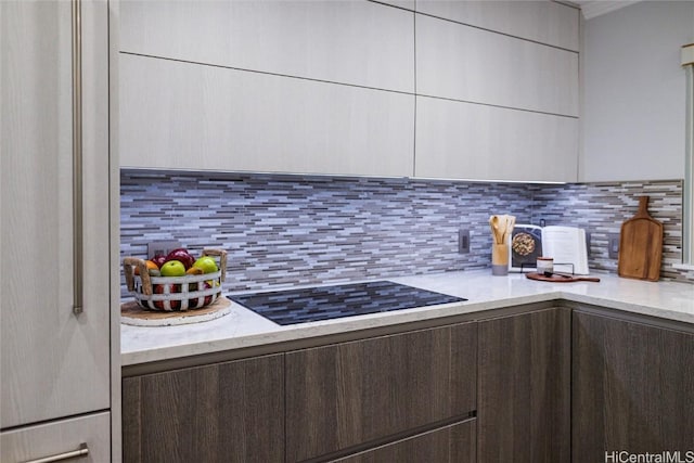 kitchen with black electric cooktop, light stone counters, decorative backsplash, and dark brown cabinets