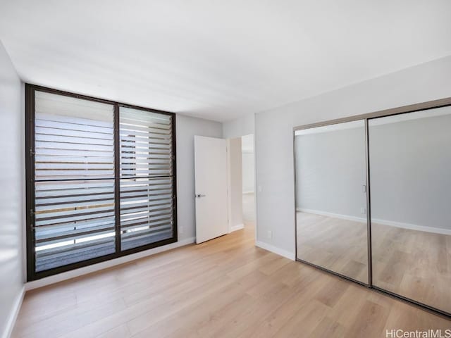 unfurnished bedroom with multiple windows, light wood-type flooring, and a closet