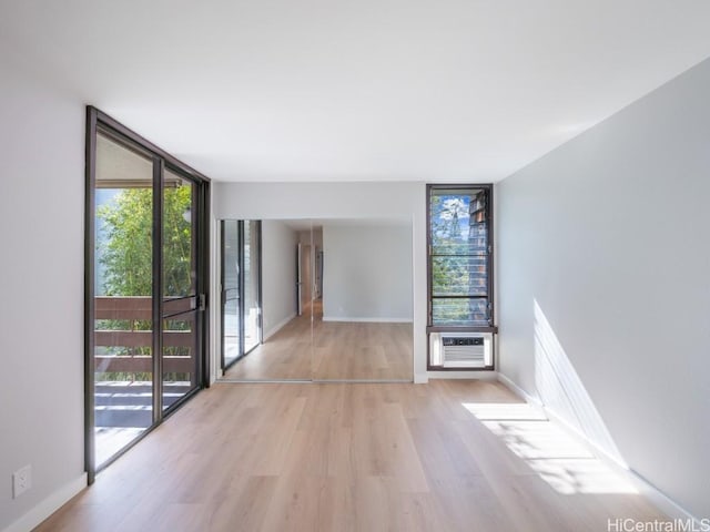 empty room featuring a wall mounted AC, light wood-type flooring, and floor to ceiling windows