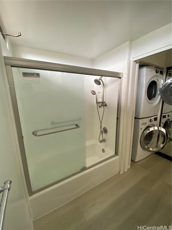 bathroom featuring hardwood / wood-style floors, enclosed tub / shower combo, and stacked washer / drying machine