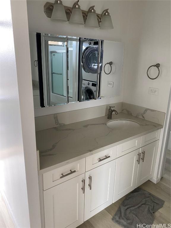 bathroom with hardwood / wood-style flooring, vanity, and stacked washing maching and dryer