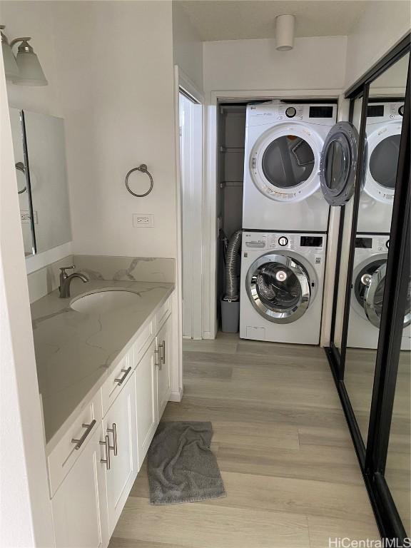 clothes washing area featuring stacked washer and dryer, light hardwood / wood-style floors, and sink