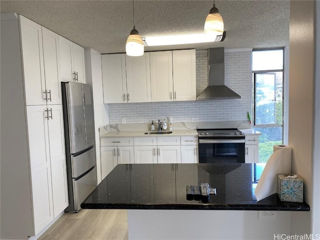 kitchen featuring decorative light fixtures, white cabinetry, wall chimney range hood, and appliances with stainless steel finishes