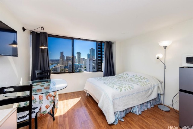 bedroom with hardwood / wood-style floors and stainless steel fridge