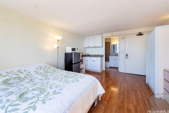 bedroom featuring dark hardwood / wood-style floors, sink, stainless steel refrigerator, and ensuite bath