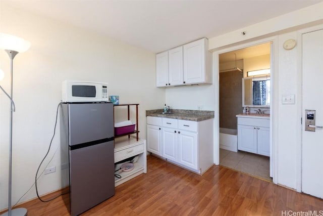 kitchen featuring light hardwood / wood-style floors, white cabinetry, sink, and stainless steel refrigerator