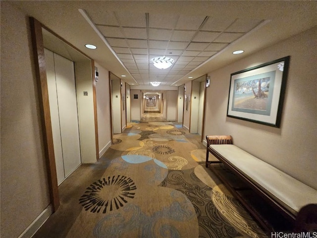 hall with a drop ceiling and light colored carpet