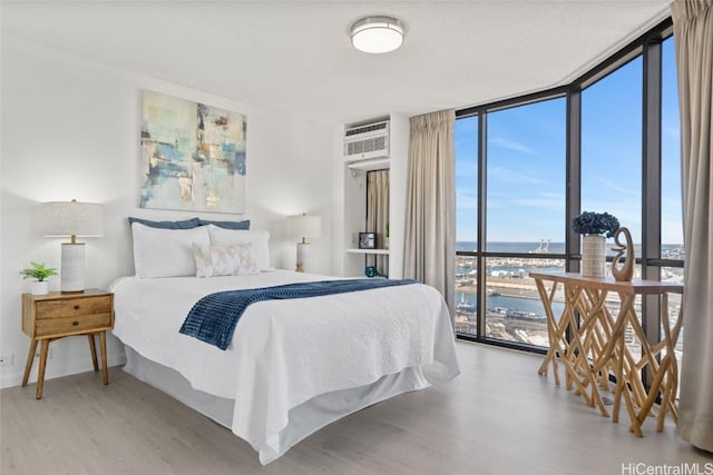 bedroom with a wall mounted AC, a water view, a wall of windows, and hardwood / wood-style flooring