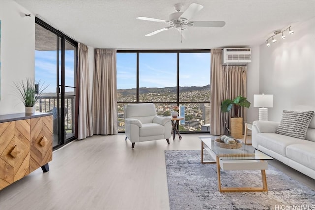 living room with ceiling fan, light hardwood / wood-style flooring, a textured ceiling, and a wall of windows