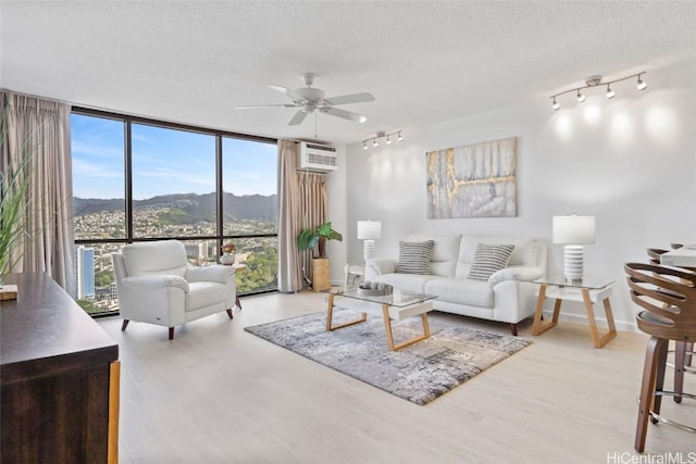 living room featuring light wood-type flooring, floor to ceiling windows, a textured ceiling, ceiling fan, and a mountain view