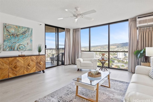 living room featuring expansive windows, a textured ceiling, a wall unit AC, ceiling fan, and light hardwood / wood-style flooring