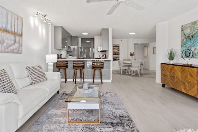 living room with ceiling fan, a textured ceiling, and light hardwood / wood-style flooring