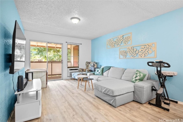 living room featuring light hardwood / wood-style flooring, a wall mounted air conditioner, and a textured ceiling