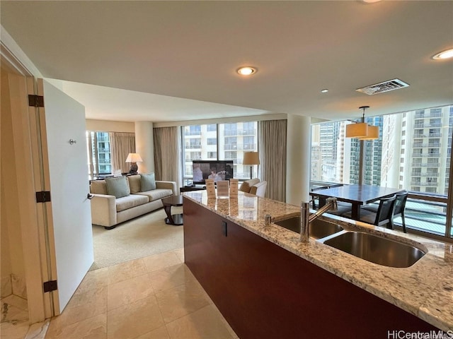 kitchen with light stone countertops, light carpet, hanging light fixtures, and sink