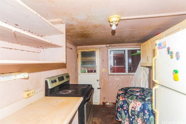 kitchen with stainless steel electric stove, cream cabinets, and white fridge