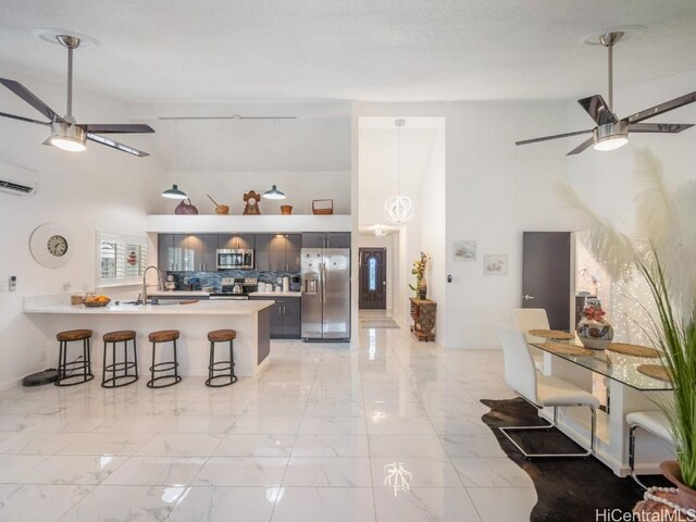 kitchen featuring a wall mounted air conditioner, sink, appliances with stainless steel finishes, decorative light fixtures, and a kitchen bar