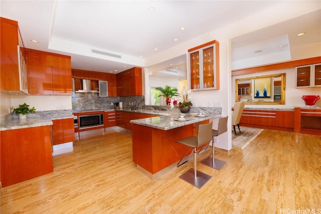 kitchen with oven, a raised ceiling, light hardwood / wood-style flooring, wall chimney exhaust hood, and kitchen peninsula