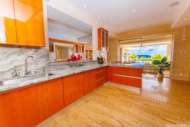 kitchen with decorative backsplash, light stone counters, kitchen peninsula, and sink