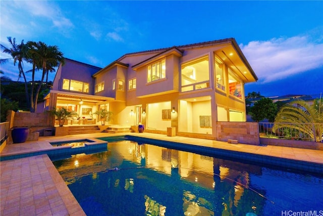 pool at dusk featuring an in ground hot tub and a patio