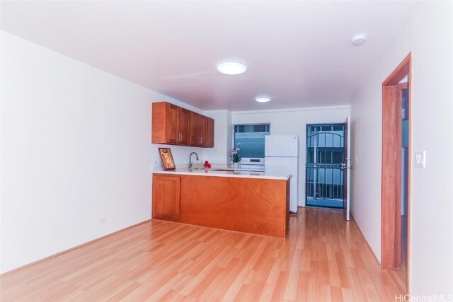 kitchen featuring sink, light hardwood / wood-style flooring, white refrigerator, kitchen peninsula, and range