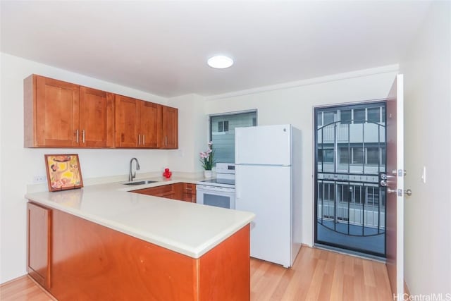 kitchen with kitchen peninsula, sink, light hardwood / wood-style floors, and white appliances