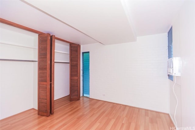 unfurnished bedroom featuring hardwood / wood-style flooring, brick wall, and a closet