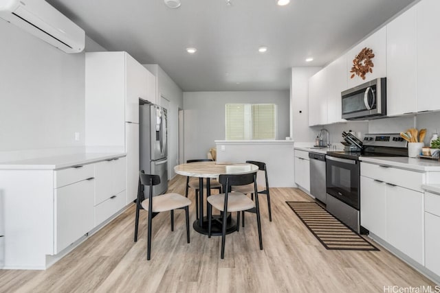 kitchen with white cabinetry, sink, light hardwood / wood-style flooring, an AC wall unit, and appliances with stainless steel finishes