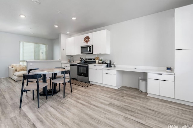 kitchen with kitchen peninsula, appliances with stainless steel finishes, sink, light hardwood / wood-style floors, and white cabinetry