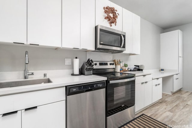 kitchen featuring white cabinets, appliances with stainless steel finishes, light wood-type flooring, and sink