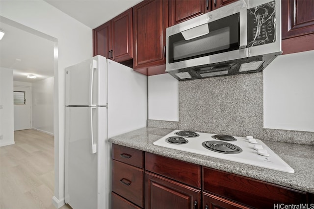 kitchen featuring tasteful backsplash, light stone countertops, light hardwood / wood-style flooring, and white appliances