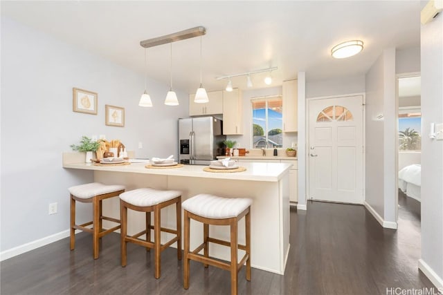 kitchen featuring stainless steel fridge with ice dispenser, kitchen peninsula, pendant lighting, a breakfast bar area, and white cabinets