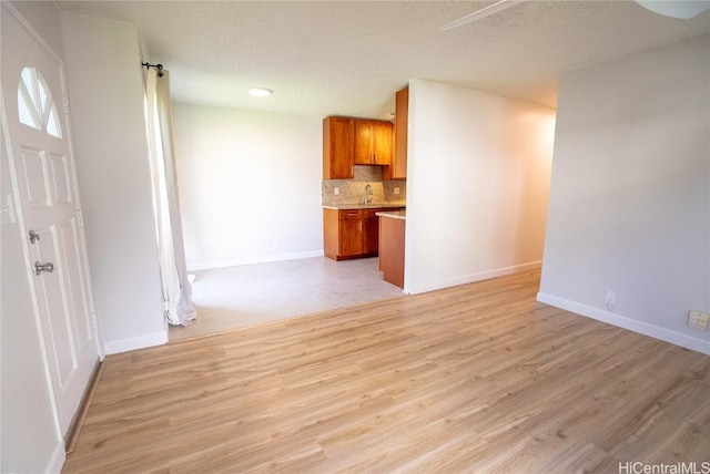 unfurnished living room with a textured ceiling, light wood-type flooring, and sink