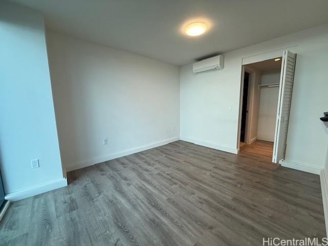 unfurnished bedroom with a walk in closet, dark wood-type flooring, a wall unit AC, and a closet