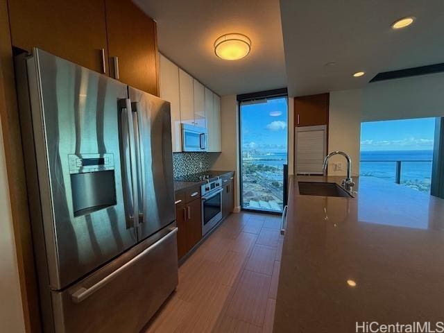 kitchen with backsplash, white cabinets, a water view, sink, and stainless steel appliances