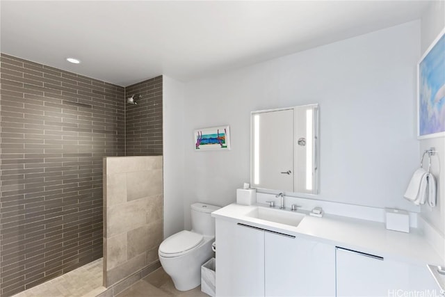 bathroom with tile patterned flooring, vanity, toilet, and a tile shower