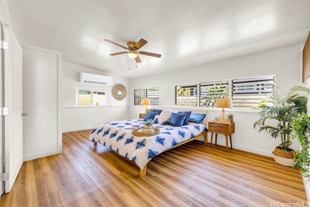 bedroom featuring light wood-type flooring, a wall unit AC, and ceiling fan