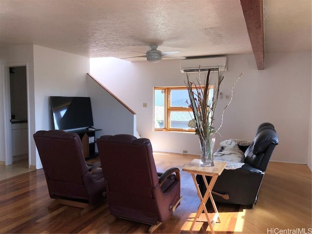 living room featuring a wall mounted air conditioner, a textured ceiling, ceiling fan, beamed ceiling, and hardwood / wood-style floors